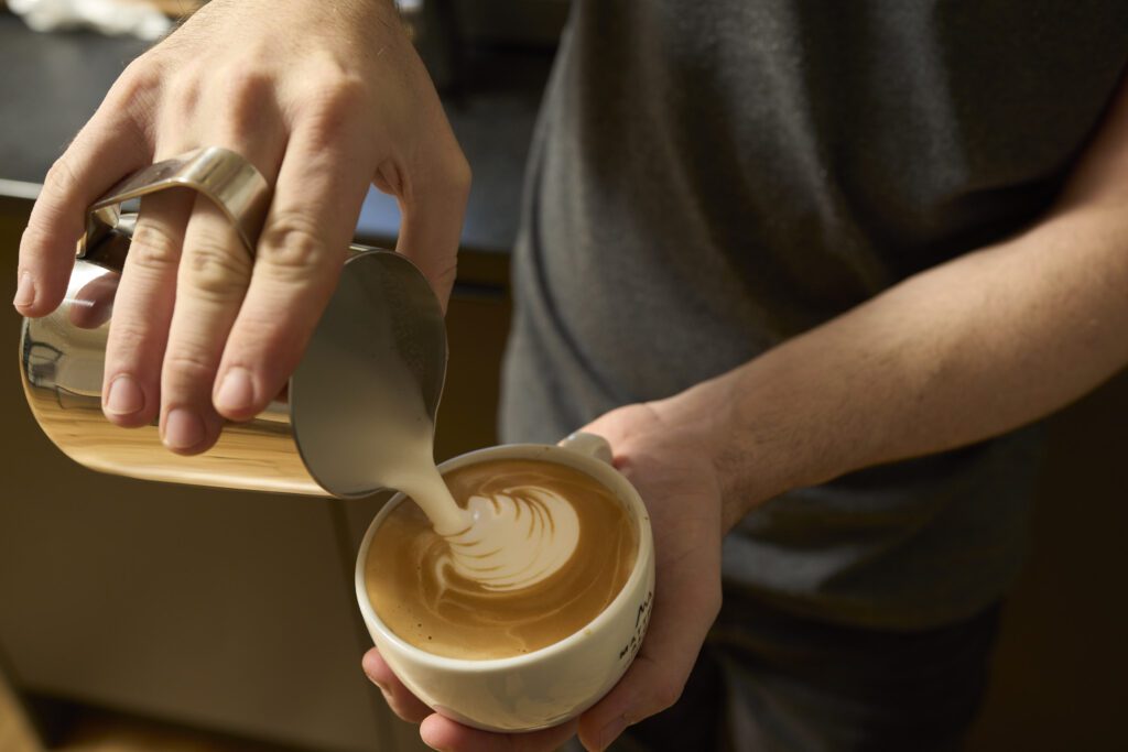 Hand pouring freshly steamed flat milk to make a latte