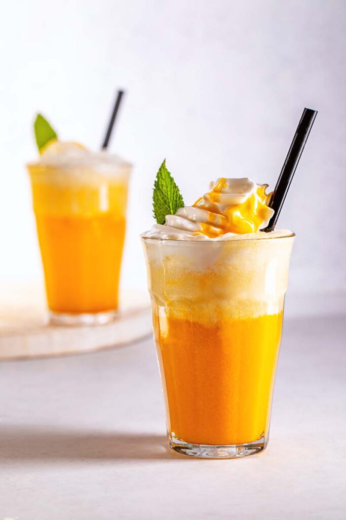 Coconut and mango cooler topped with whipped cream, mint leaf and a straw