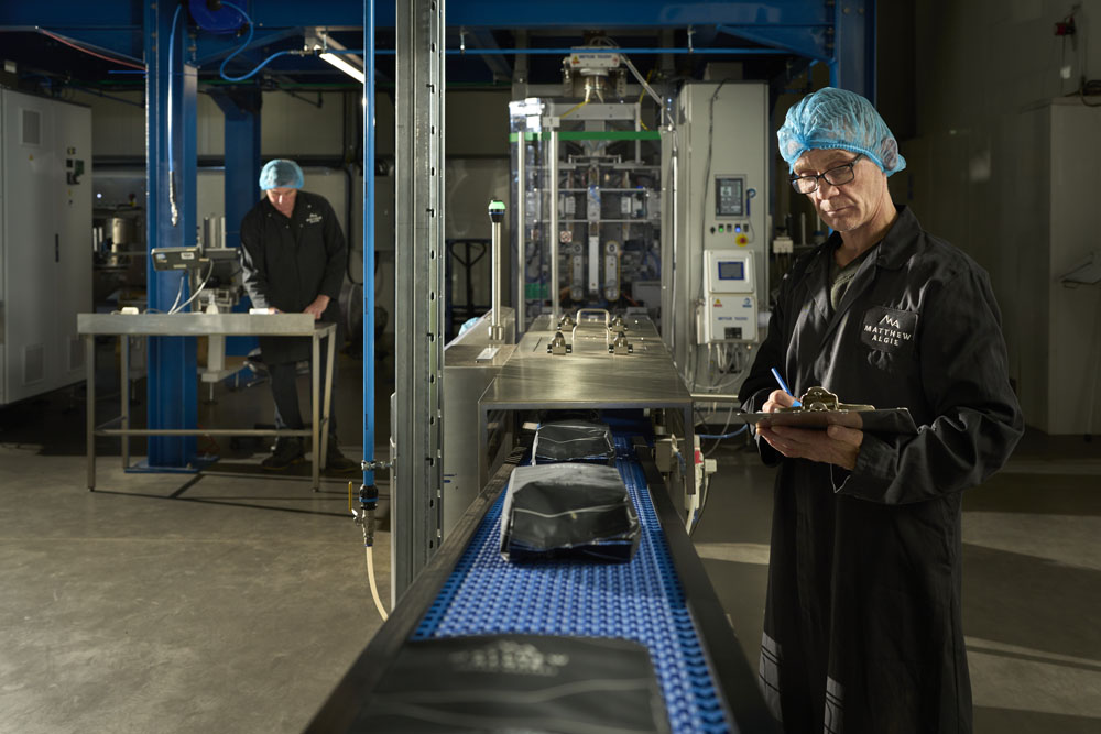 Two employees working in the Matthew Algie coffee roastery on the coffee packaging line.